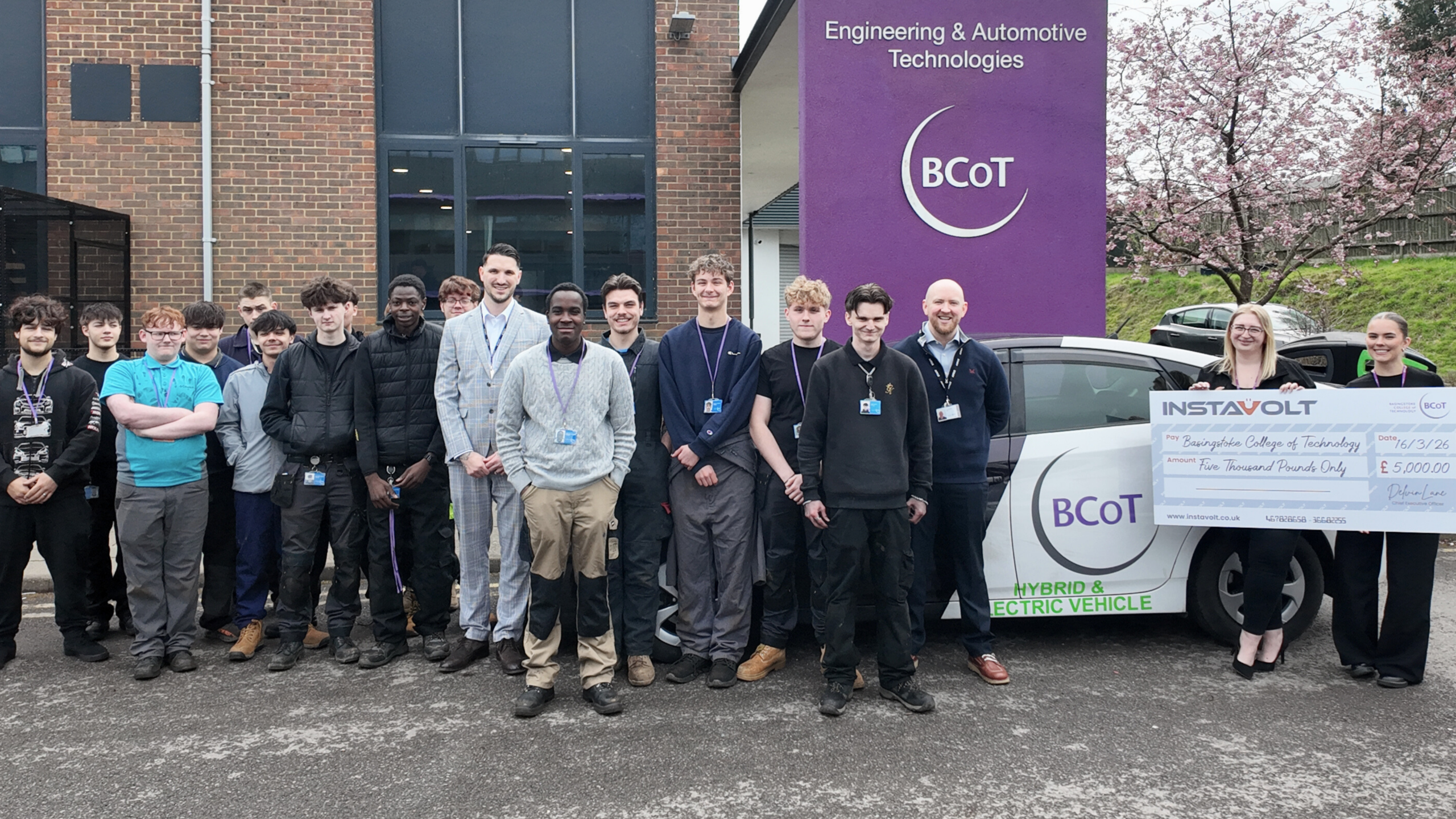 InstaVolt presents £5,000 donation to BCoT engineering and automotive students, standing with staff and learners beside a hybrid and electric vehicle training car outside the college.