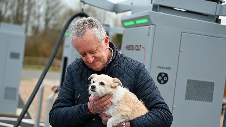 Man holding a small dog beside an InstaVolt ultra rapid EV charging station in a rural outdoor setting